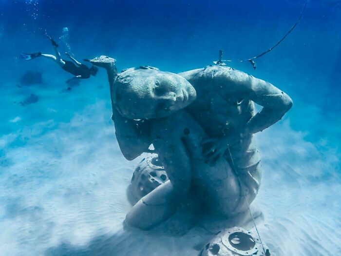 Underwater photo of a large ocean statue with a diver swimming nearby, showcasing unexpected ocean photos.