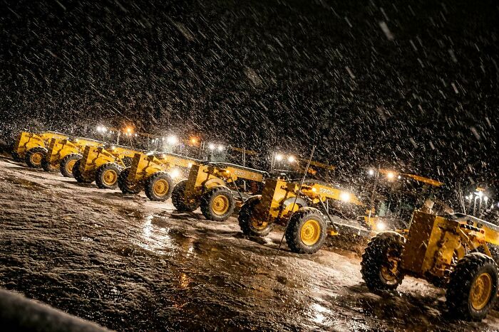 A line of yellow snowplows illuminated at night during a heavy snowfall, representing the hard work of a great dad.