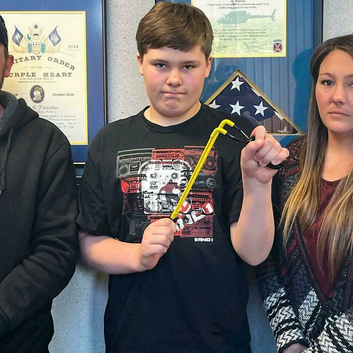 Boy holding broken slingshot standing with adults in front of military awards
