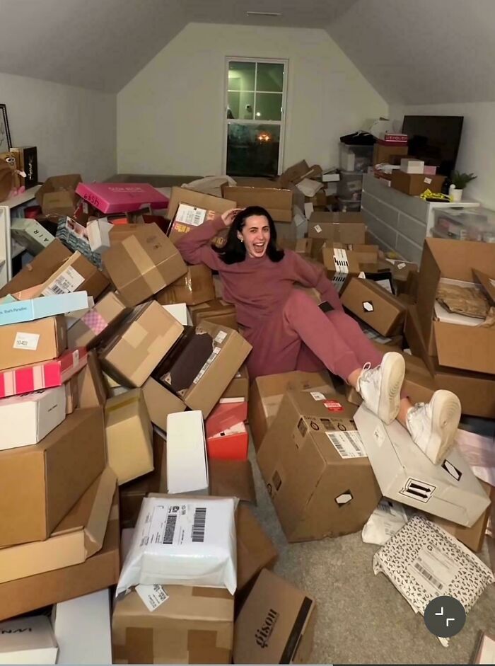 Woman in casual clothes surrounded by numerous cardboard boxes and packages illustrating consumerism excess.