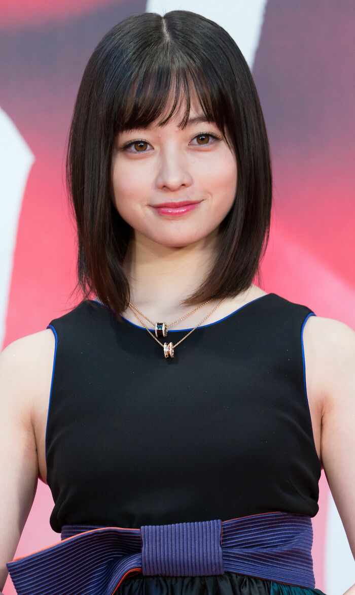 Kanna Hashimoto smiling with shoulder-length hair, wearing a black dress and layered necklaces at an event.