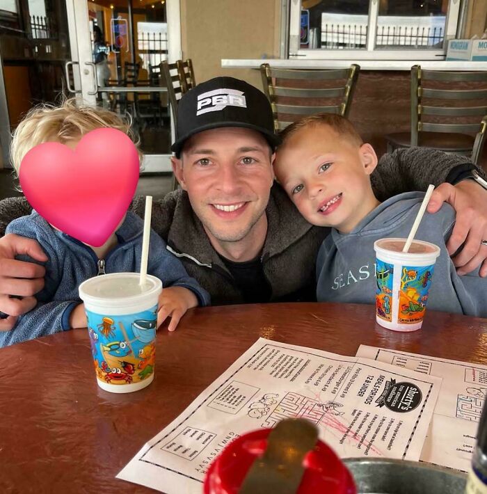 A great dad smiling with his two young sons at a restaurant, enjoying a family meal together, exemplifying a great dad.