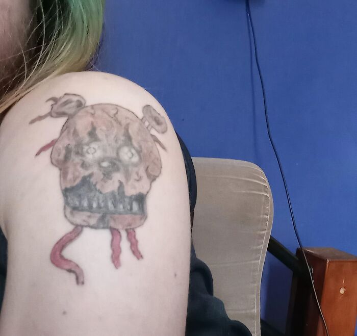 Tattoo of a distorted skull with hanging ribbons on a shoulder showcasing bad tattoos proving thinking first is optional.