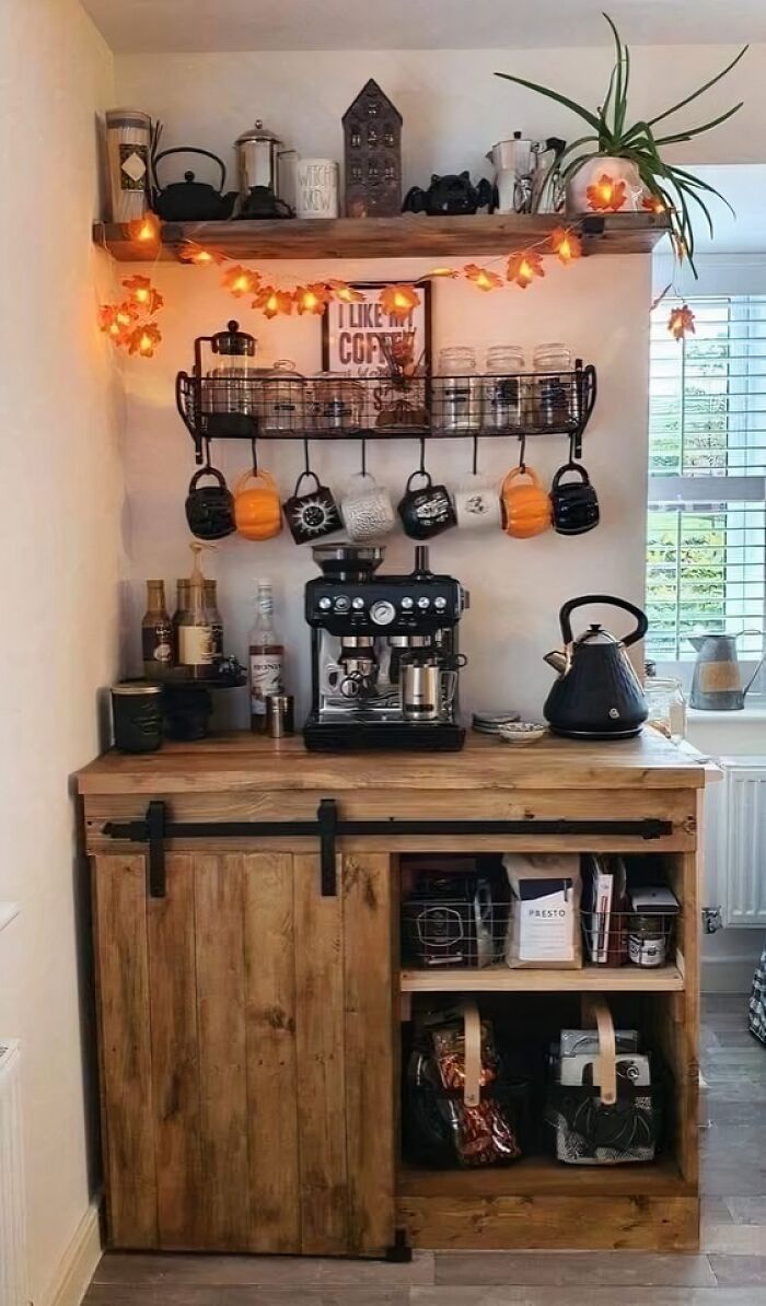 Cozy coffee station with wooden cabinetry and shelves, featuring warm lighting and a collection of mugs and coffee accessories.
