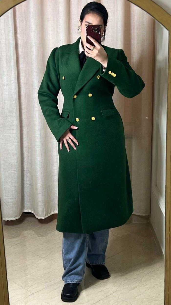 Person taking a mirror selfie wearing a green double-breasted coat and jeans, showcasing a DIY fashion win.