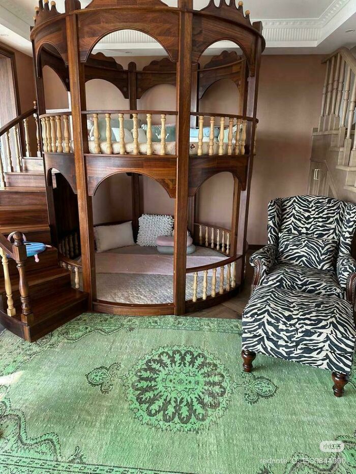Wooden two-level bunk bed with staircase next to a zebra print armchair and green patterned rug in living room.