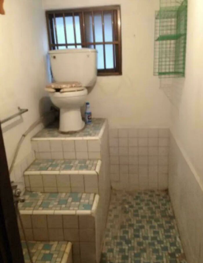 Toilet placed on a tiled platform with stairs in a narrow bathroom, an example of ridiculous home decor and DIY.