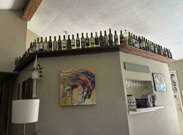 Ridiculous home decor with dozens of empty wine bottles lined up on a high wooden shelf in a living room.