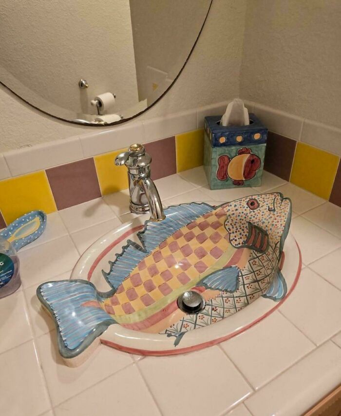 Colorful fish-shaped ceramic sink in bathroom with quirky home decor and DIY elements on tiled countertop.