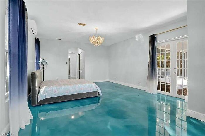 Spacious bedroom with blue epoxy floor reflecting light, minimalist decor, and large windows showcasing unique home decor.