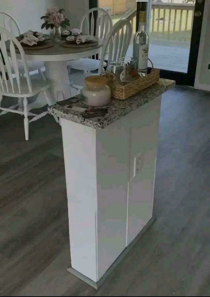 Narrow kitchen island with granite top, holding a tray with bottles and glasses, in a dining area with white chairs.