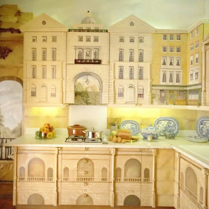 Kitchen with ridiculous home decor featuring building facade designs on cabinets and walls with pots and dishes displayed.