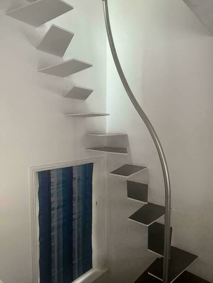 Minimalist floating staircase with narrow steps and a curved metal handrail in a small white-walled space, showcasing ridiculous home decor.
