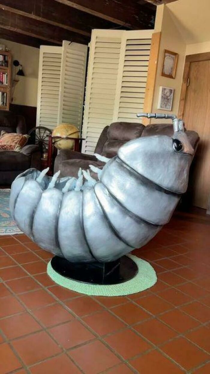 Ridiculous home decor featuring a large silver bug-shaped chair in a living room with rustic furniture.