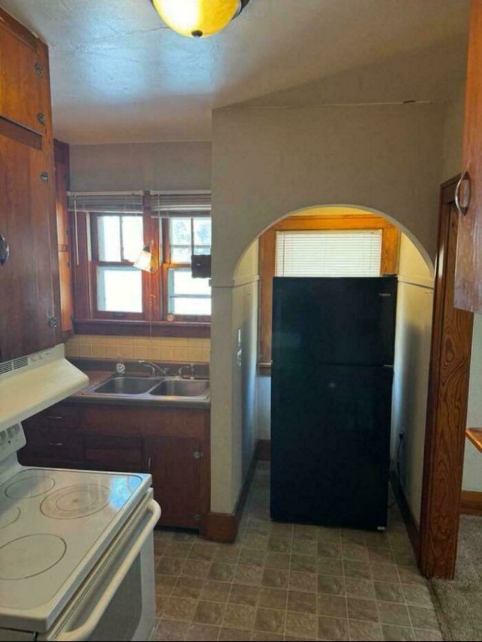 Small kitchen with a black refrigerator awkwardly placed under an archway, showcasing ridiculous home decor and DIY fail.
