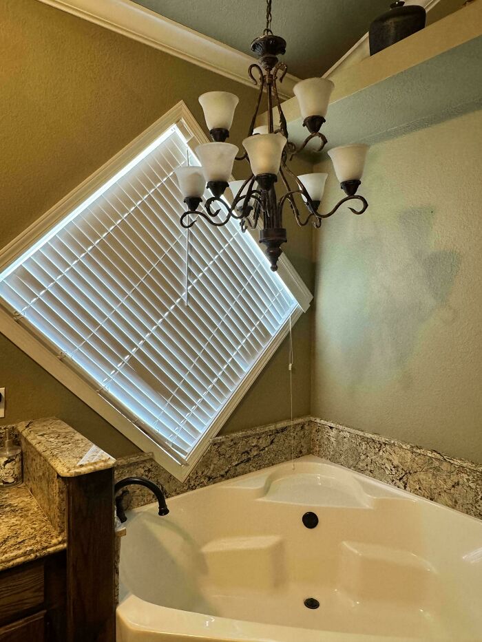 Bathroom with a tilted window blind, chandelier, and bathtub showcasing ridiculous home decor and DIY design fail.