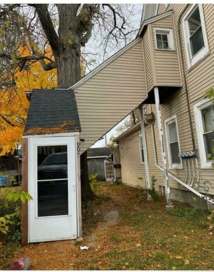 Narrow enclosed stairway with awkward home decor and DIY design under autumn trees between houses.
