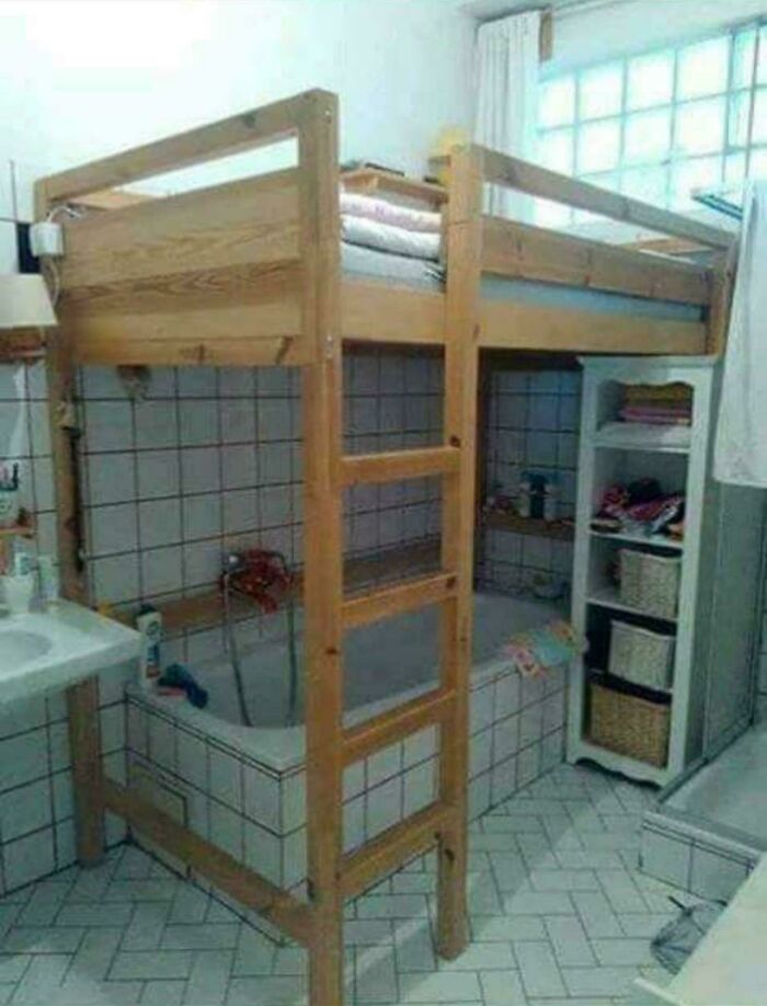 Wooden loft bed built over a bathtub in a tiled bathroom, an example of ridiculous home decor and DIY with funny style.