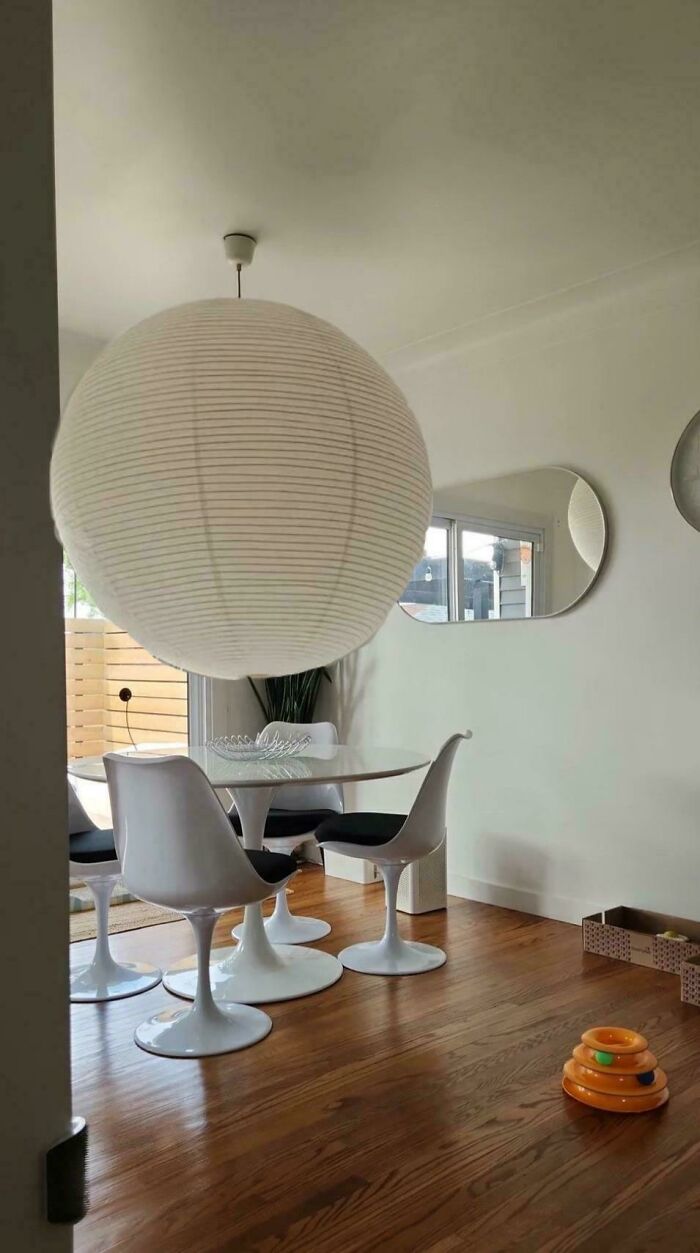 Modern dining room with white tulip chairs and table, featuring a large round paper lamp and playful home decor elements.