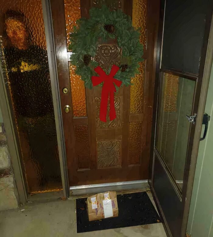 Delivery confirmation pic showing a package left on a doorstep decorated with a holiday wreath and bow.