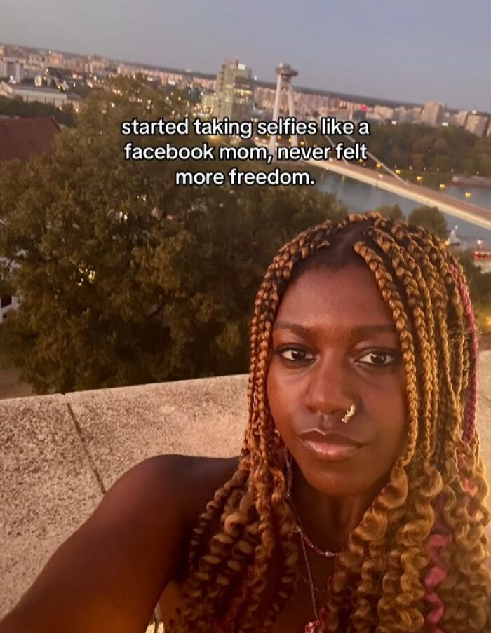 Woman with braided hair taking a selfie outdoors at sunset, capturing the chaotic energy of a mom on social media.