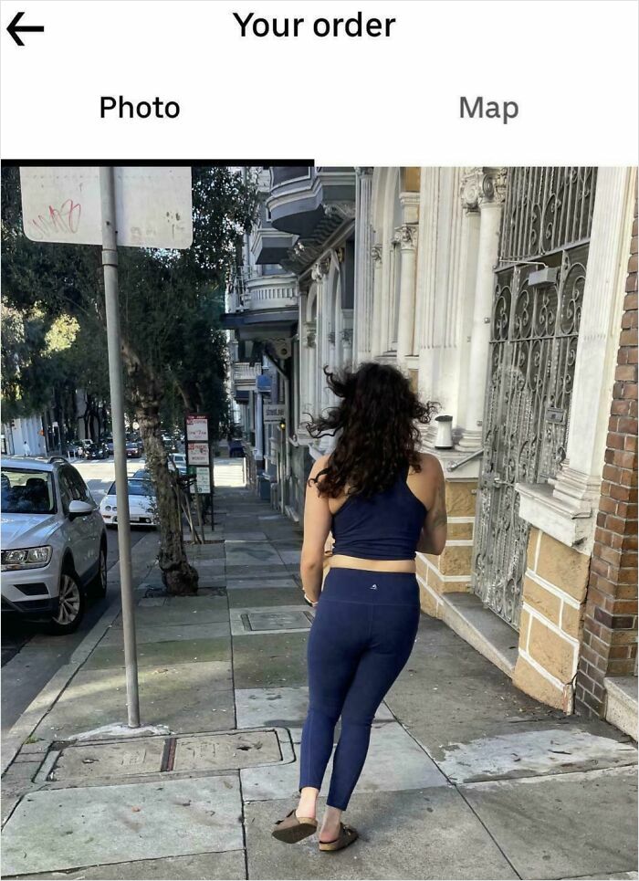 Woman walking on a city sidewalk captured in a delivery confirmation photo sent by driver to customer.