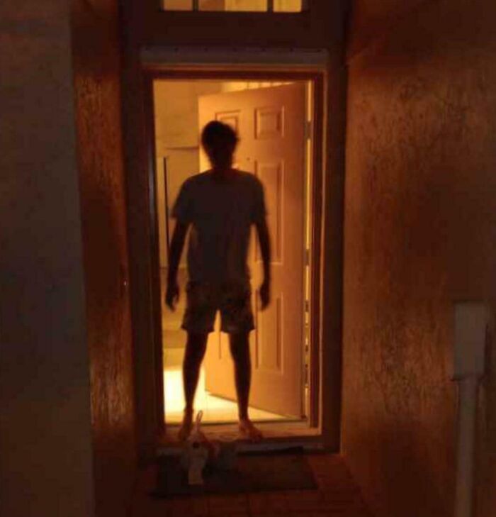 Silhouetted delivery driver standing in a doorway at night with package on the doorstep in delivery confirmation pics.