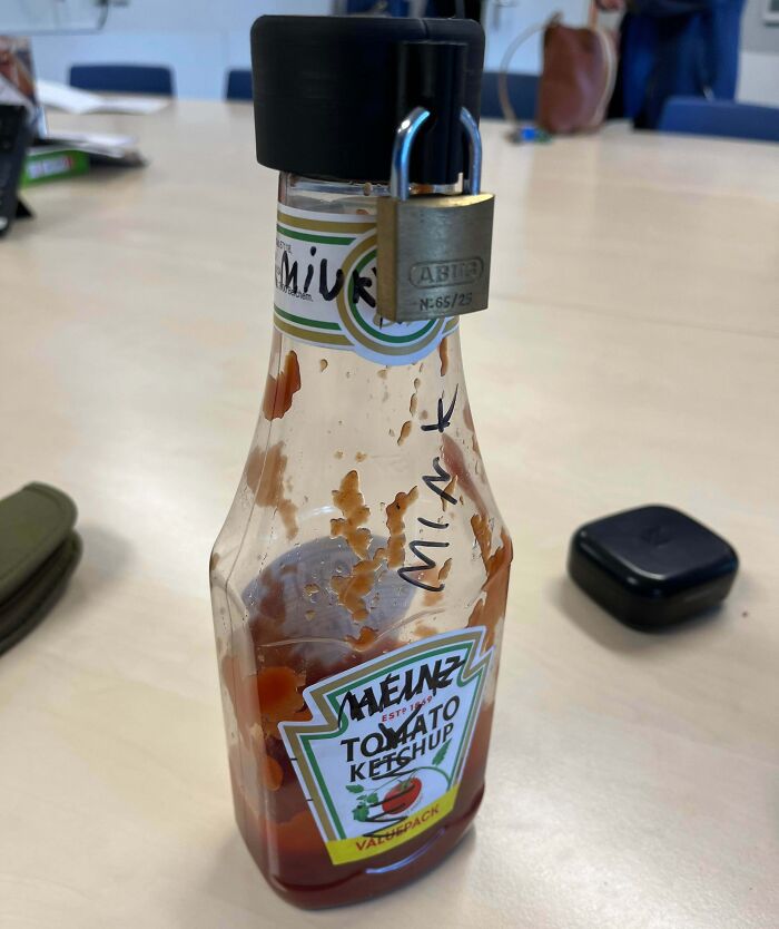 Half-empty ketchup bottle labeled with a name and secured with a padlock, illustrating selfishness in shared spaces.