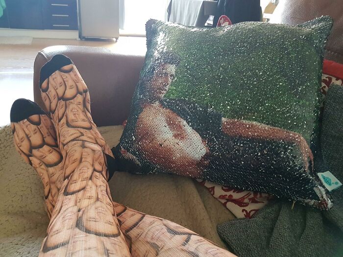 Legs wearing funny printed socks next to a sequined pillow with a humorous image, perfect for Valentine’s Day gifts.