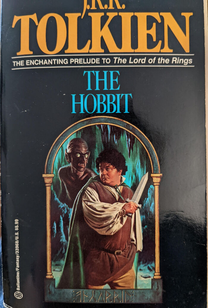 Book cover of The Hobbit by J.R.R. Tolkien featuring a man with a sword and a monstrous figure behind him.
