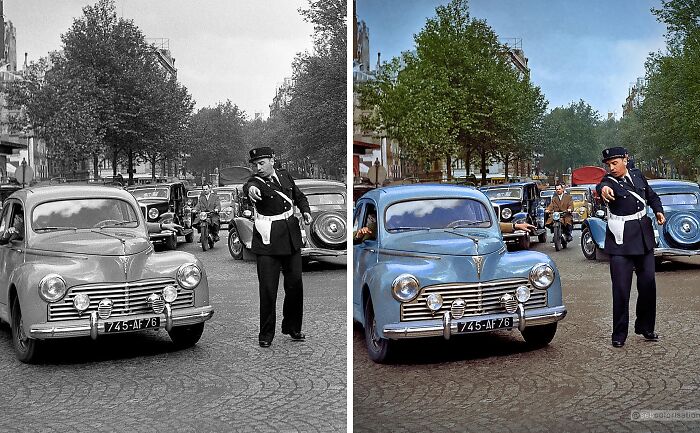 Black and colorized historic street scene by Sébastien De Oliveira showing vintage cars and a traffic officer directing vehicles.