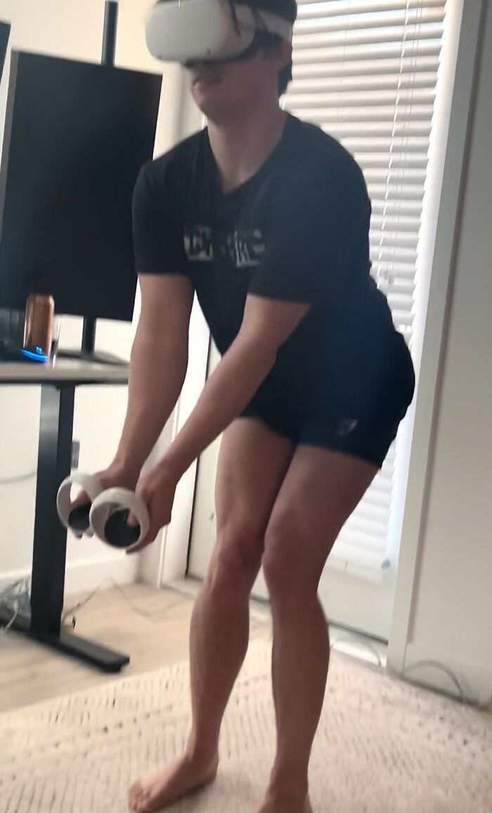 Man wearing virtual reality headset awkwardly bending forward holding controllers in a casual indoor setting showing body language.