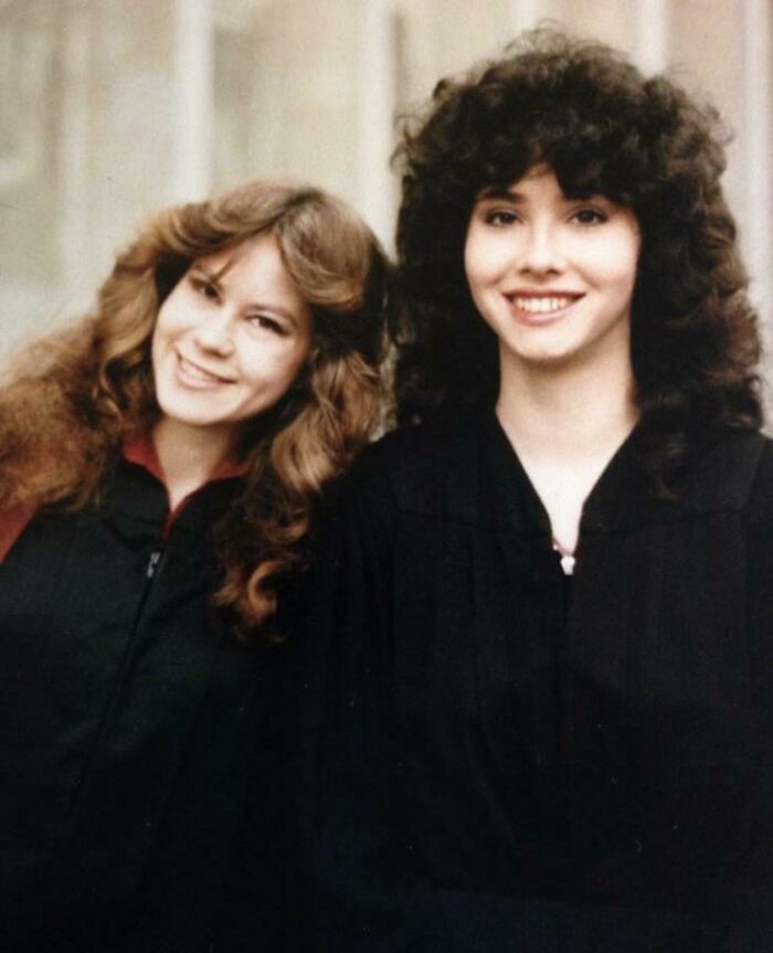 Two young women smiling with iconic 80s hairdos featuring voluminous curls and layered styles.