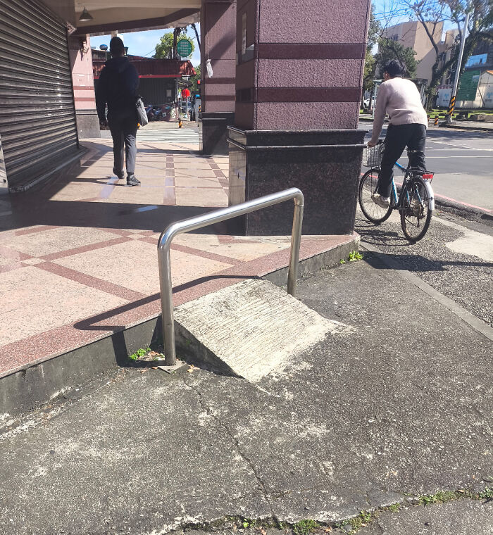 Sidewalk ramp blocked by metal railing, illustrating a classic you had one job fail and lack of common sense.