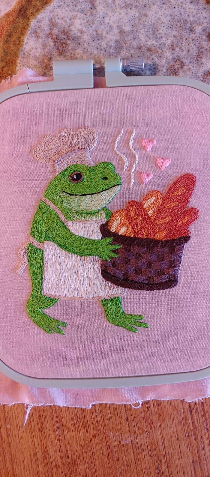 A delightful embroidery creation of a frog chef holding a basket of bread, perfect for an embroidery hobby.