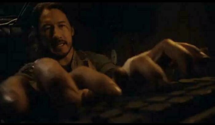 Man with long hair reaching towards a computer keyboard, highlighting absurd movie and TV details in a dark scene.