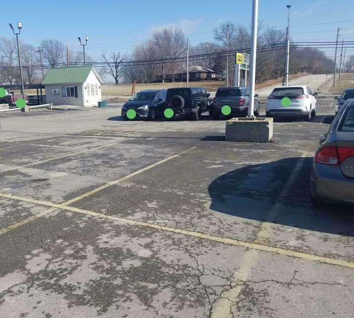 An empty parking lot with several cars, a small building, and distant trees, showcasing a design fail.