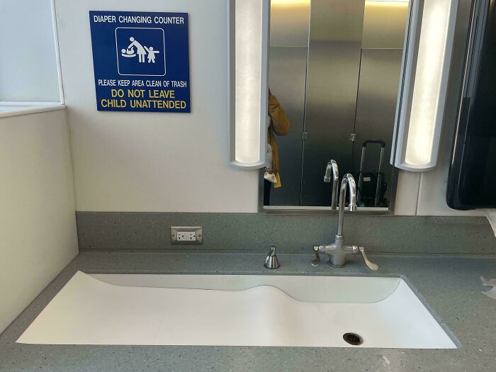 A hilariously unhinged design fail with a low sink and a sign for a diaper changing counter, warning to not leave child unattended.