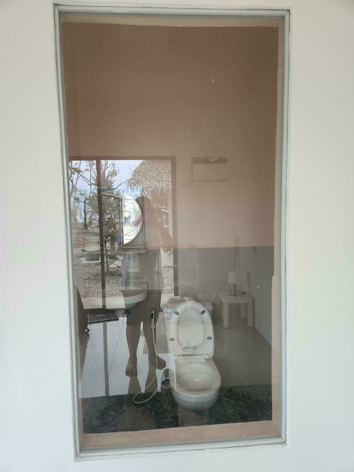 A clear glass window in a bathroom, revealing the toilet inside, a significant design fail.