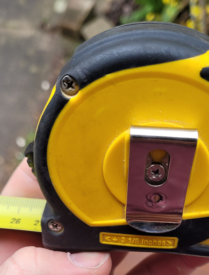 Yellow and black tape measure with a metal clip, showing a design fail where the clip is screwed over a measurement.