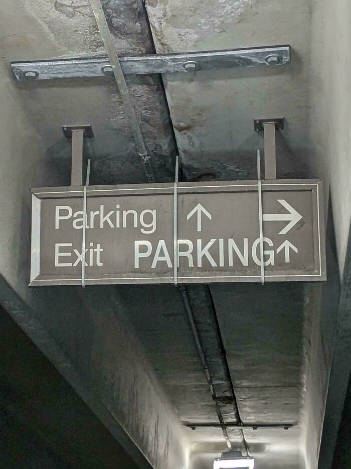 Confusing overhead sign in a parking garage with conflicting arrows and text for Parking and Exit, a design fail.