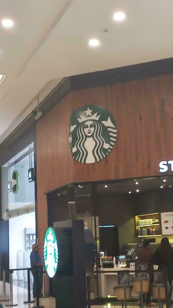 Hilariously unhinged design fail: a disfigured Starbucks logo peeling off a wooden wall in a mall setting.