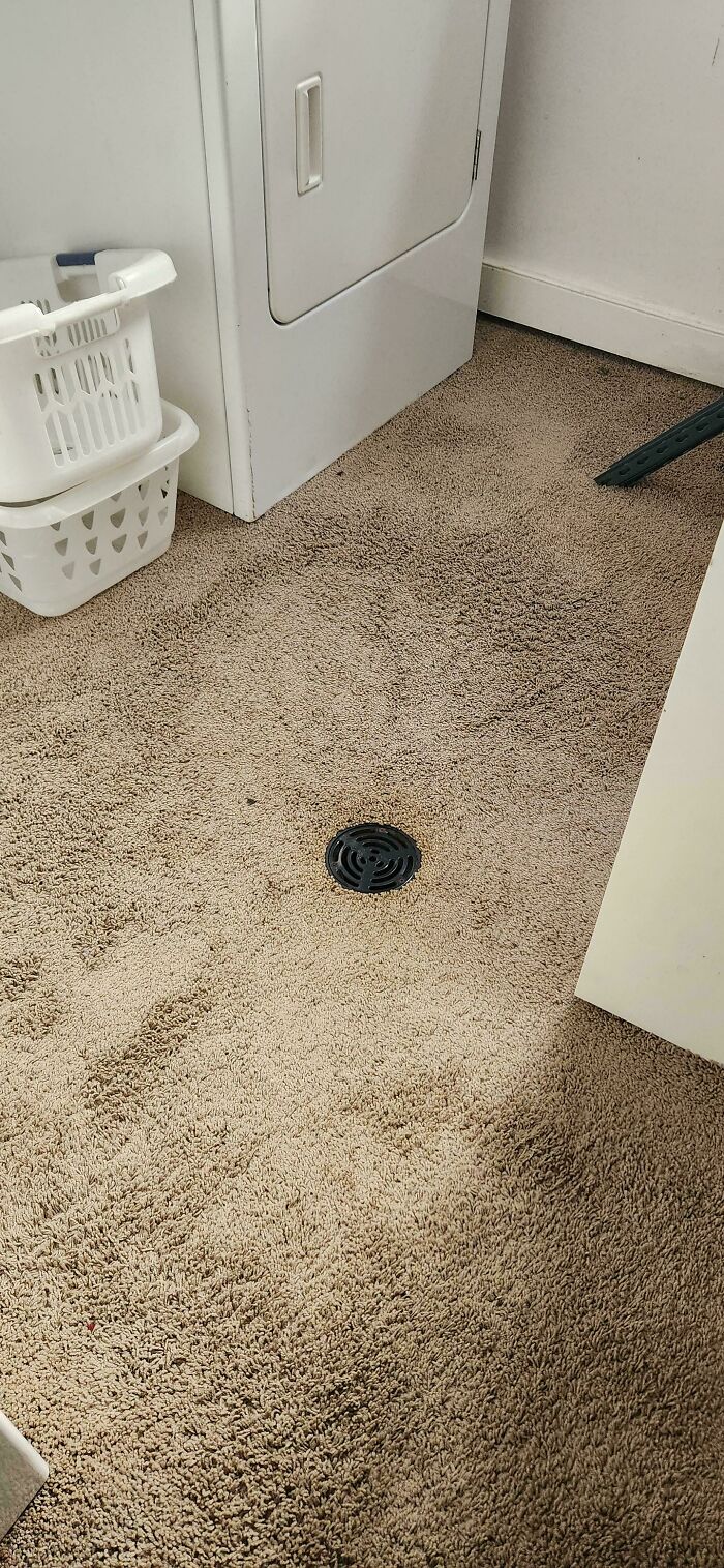 A floor drain in the middle of a carpeted room next to a washing machine, showcasing design fails.