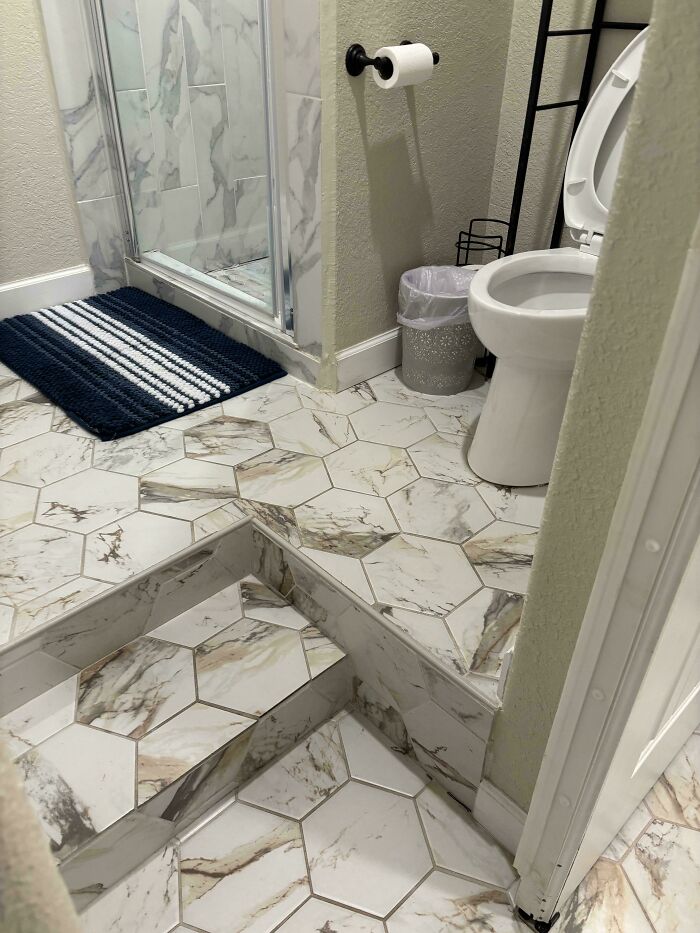 A bathroom with hexagon tile flooring and a raised platform step leading to the shower, a clear design fail.