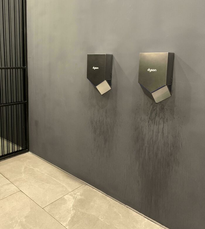 Two Dyson hand dryers on a wall with noticeable water stains underneath, showing a design fail.