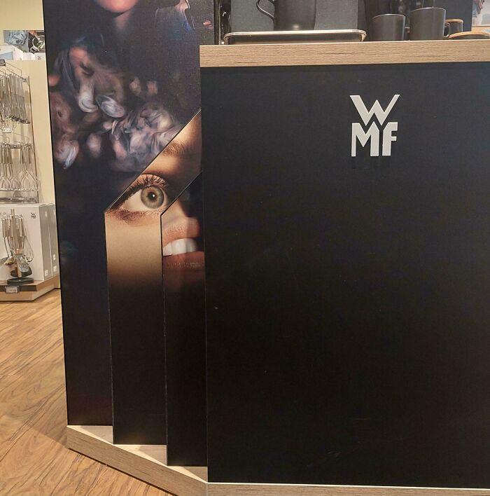 A close-up of a store display with a large image of a woman's eye and mouth, partially obscured, next to a black panel with the WMF logo, showcasing design fails.