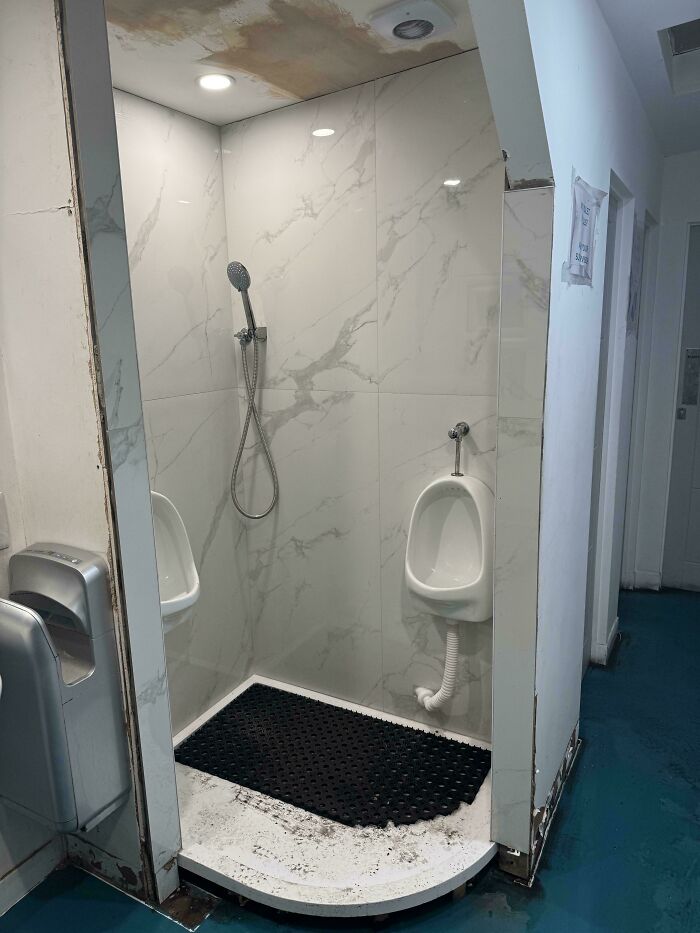 Public restroom with a shower, two urinals, and hand dryers, an unhinged design fail in public facilities.