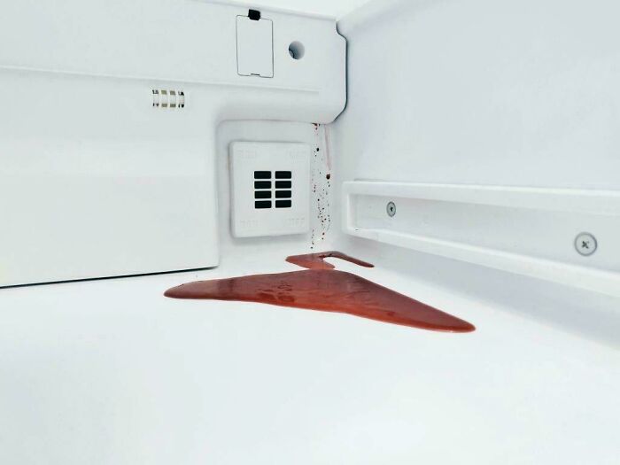 Red liquid spill inside white refrigerator interior