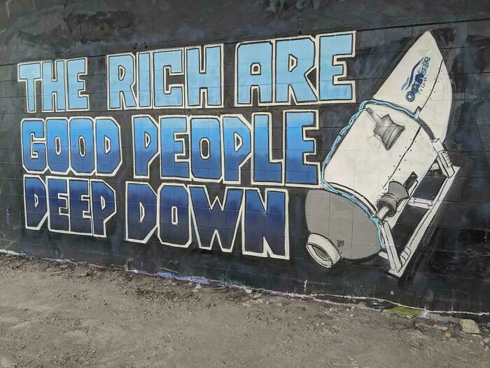 Graffiti mural with bold text The rich are good people deep down alongside a painted tilted robot on a wall.