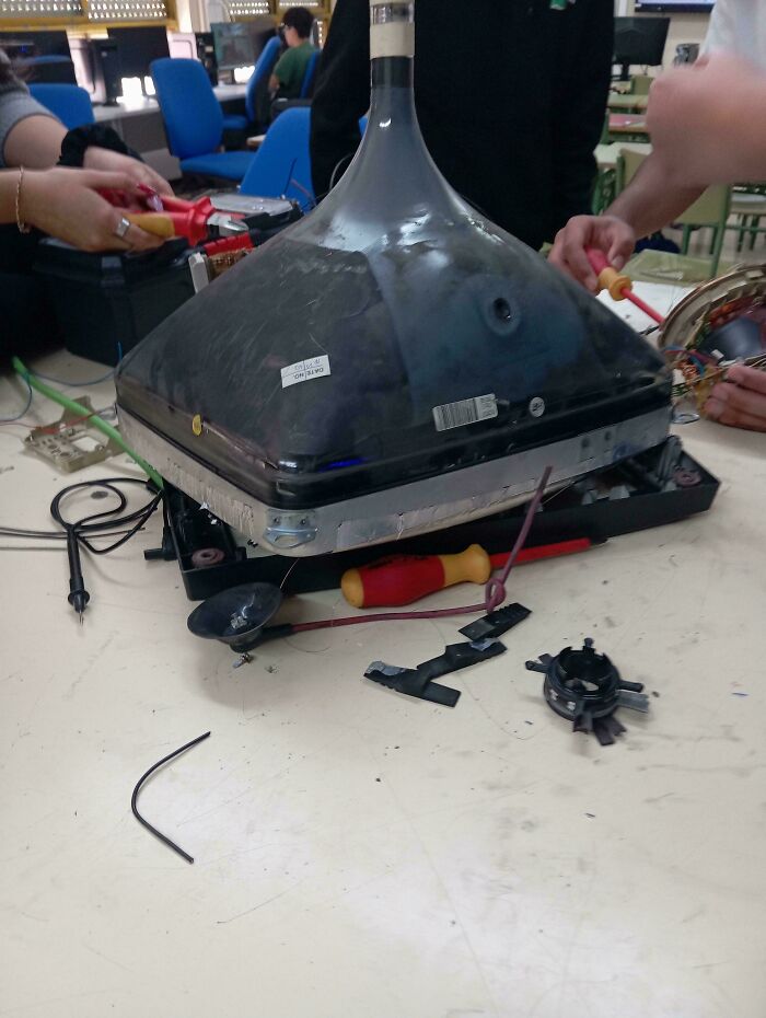 Tech support workers repairing a broken CRT monitor with tools on a cluttered white workspace.